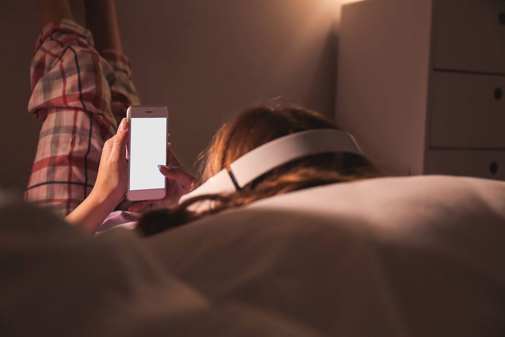 Teenage girl with mobile phone listening to music in bed