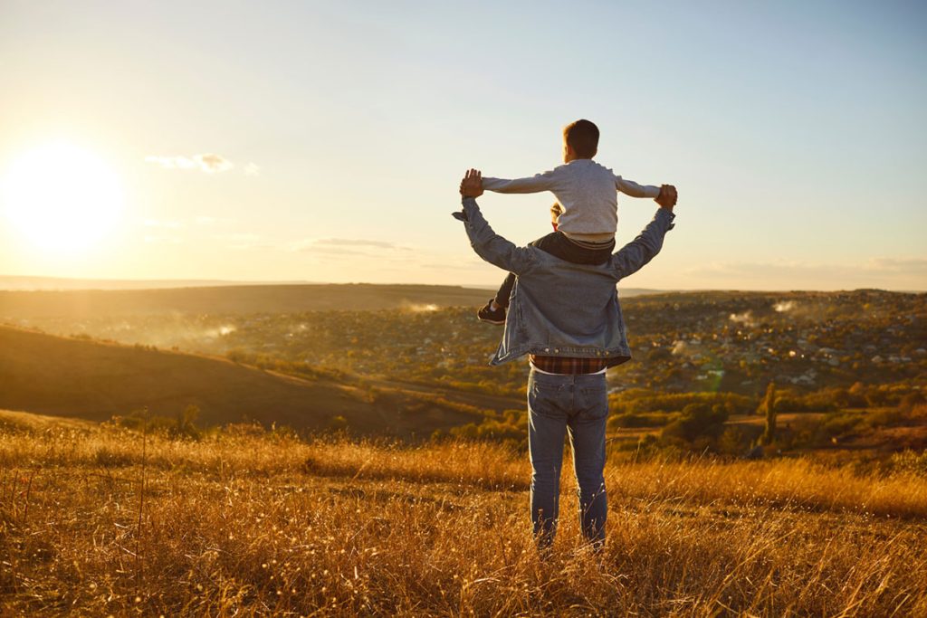 Child sitting on his father's shoulders looking at the setting sun